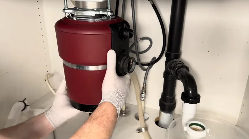 Technician clearing a dishwasher drain line at the garbage disposal connection in a Spartanburg home